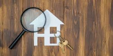 Magnifying glass over paper house with keys on wooden table.