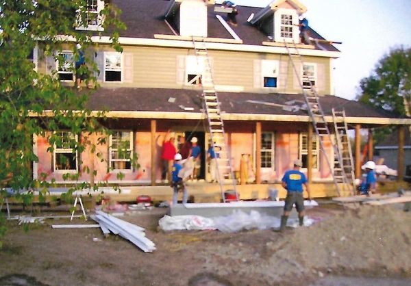 Construction workers building a large house with ladders and tools.