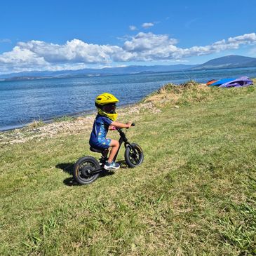 Child wearing a yellow helmet rides a bike near a lake under blue skies.