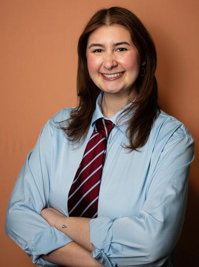 Smiling woman in blue shirt and striped tie, arms crossed.
