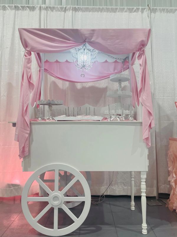 Elegant white cart draped with pink fabric and a chandelier above.