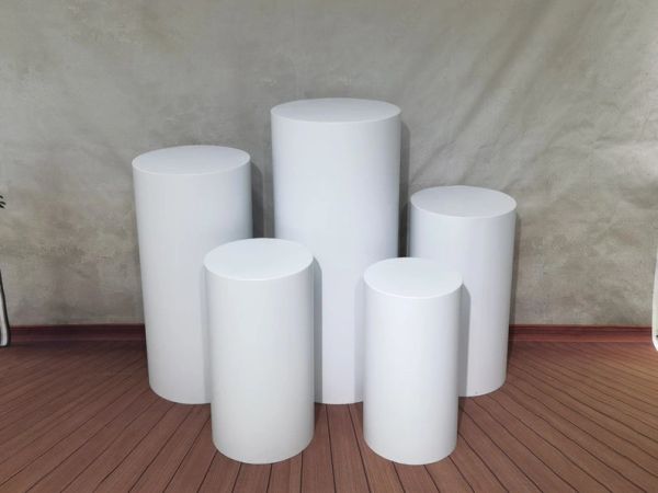 Five white cylindrical pedestals of varying heights on a wooden floor.