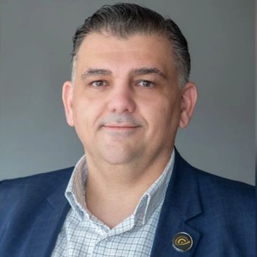 Professional man in a blue suit jacket and checked shirt with a pin on his lapel.