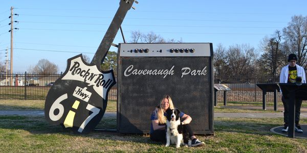 Large guitar and amplifier sculpture at Cavenaugh Park with a woman and dog.