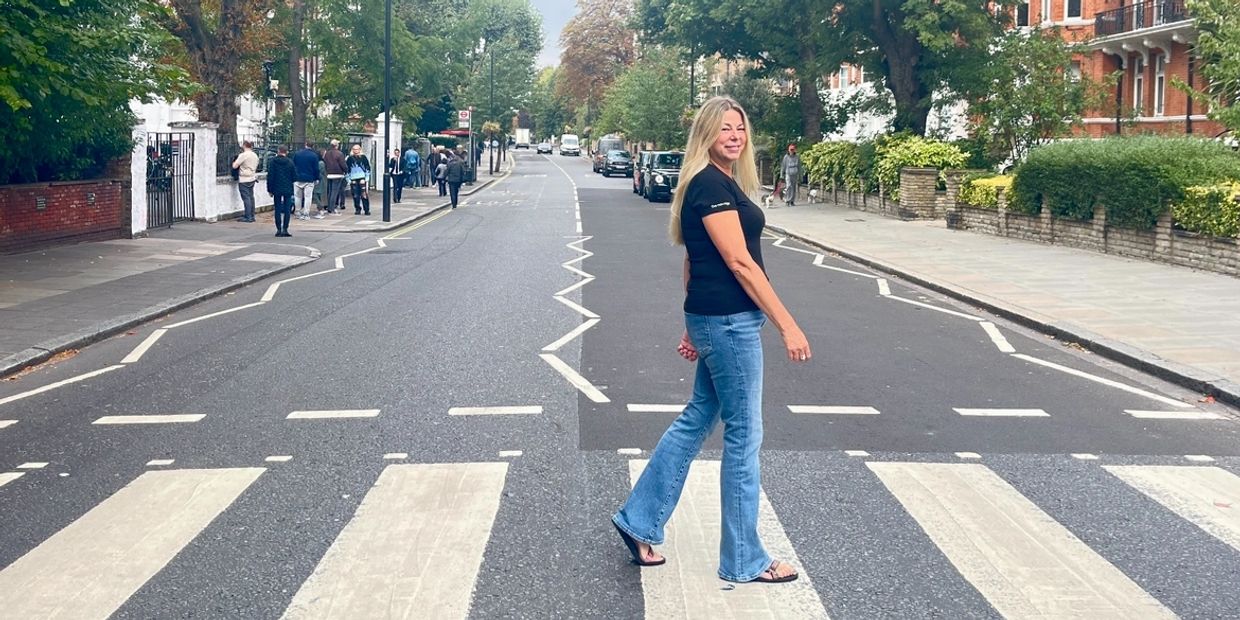 Woman walking across a famous zebra crossing with people waiting in the background.