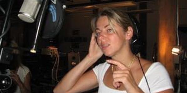 Woman recording vocals in a music studio with headphones and microphone.