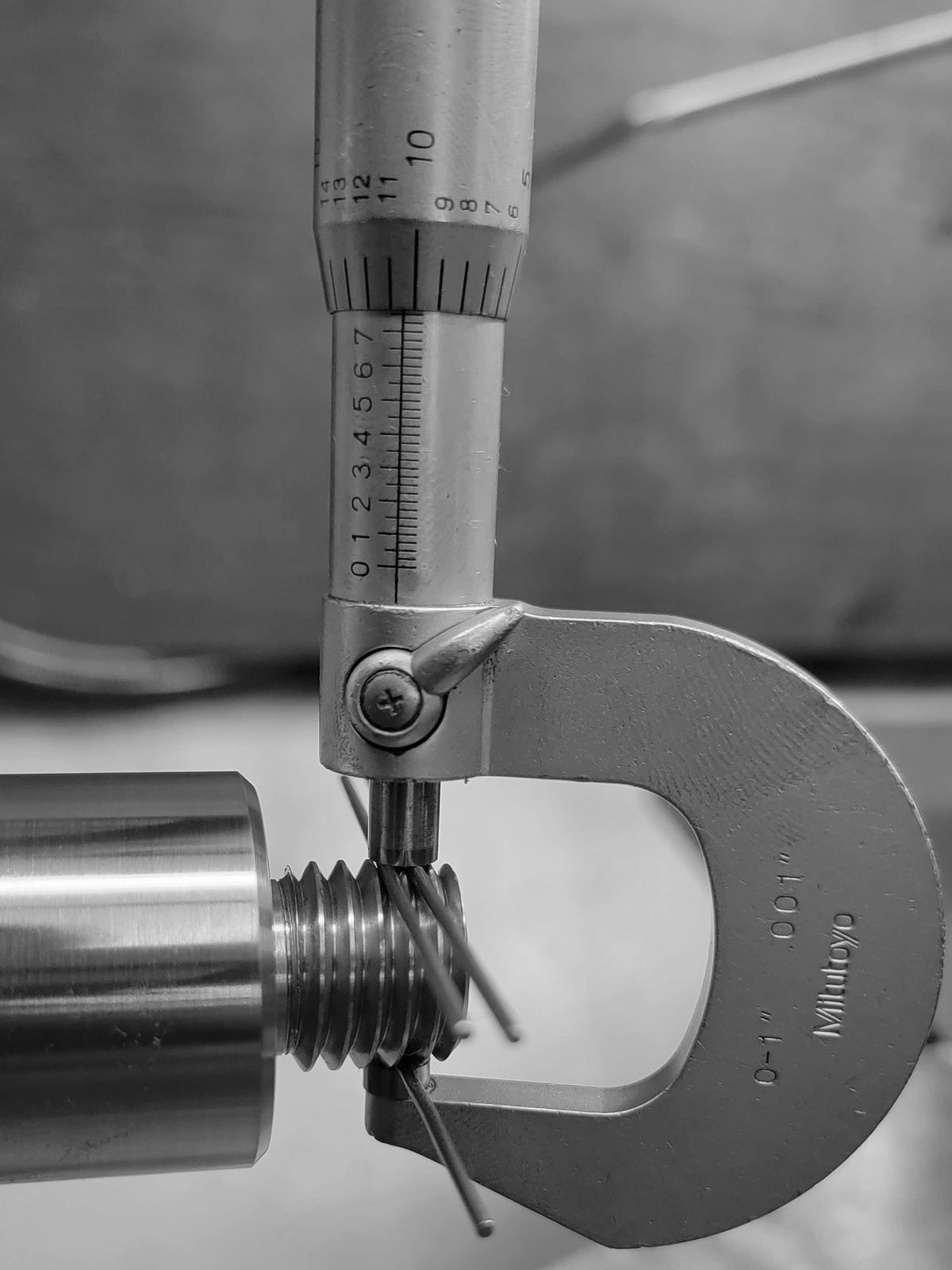 Close-up of a micrometer measuring a threaded metal part.