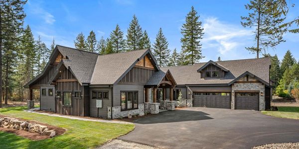 Modern rustic house with stone accents and a spacious driveway surrounded by trees.