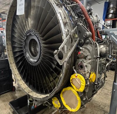 A large aircraft jet engine on a workshop floor, partially covered components.