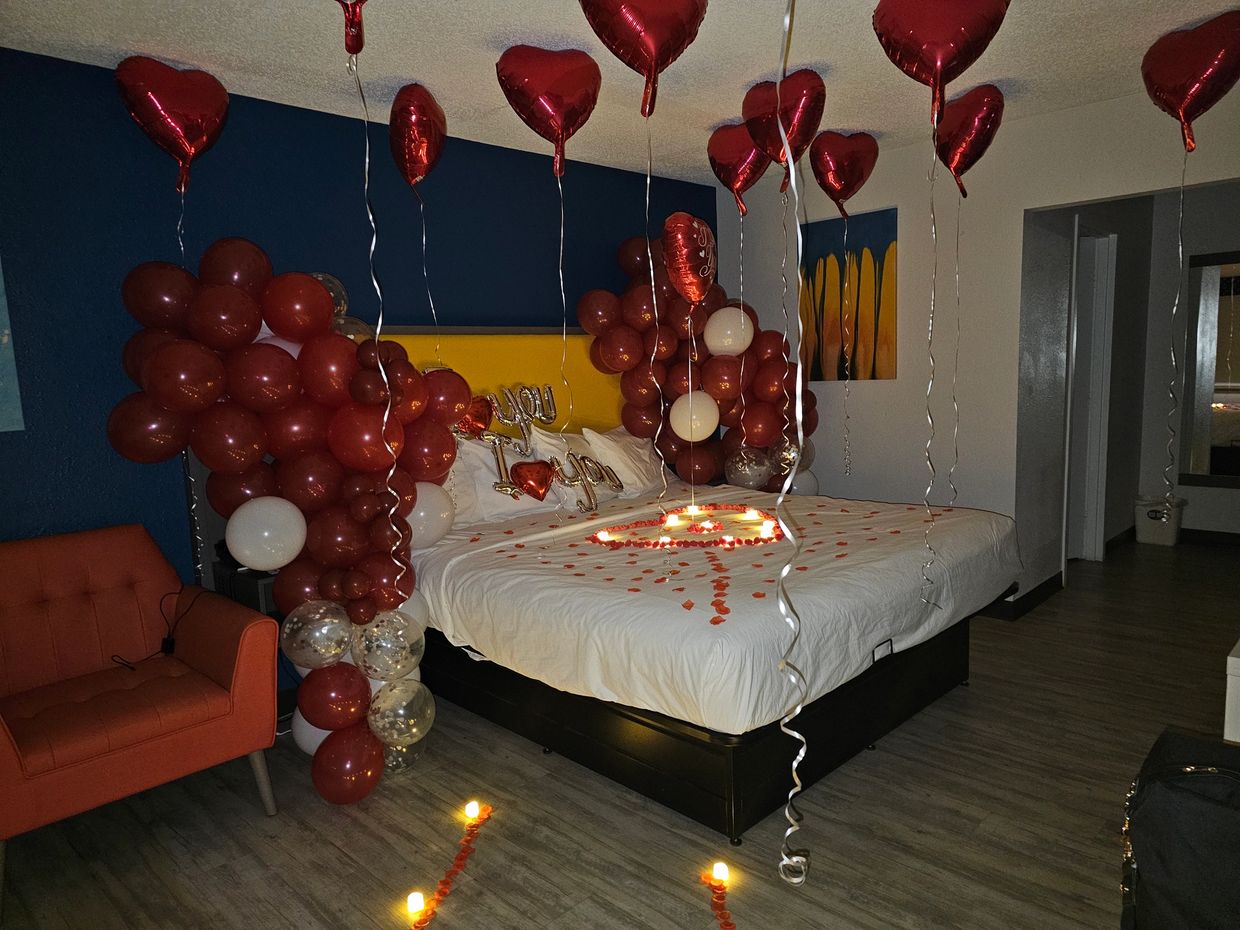 A hotel room decorated with heart-shaped red foil balloons and red balloon cluster columns 