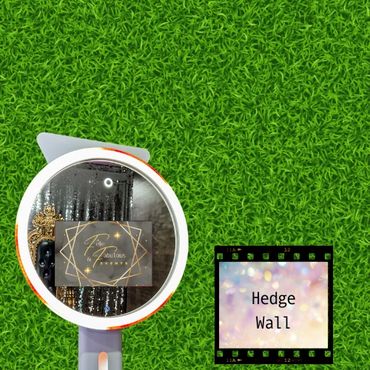 A selfie ring light mirror photo booth in front of a green hedge wall backdrop.