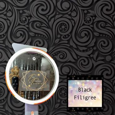 A selfie ring light mirror photo booth in front of a black filigree backdrop.