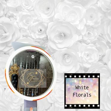 A selfie ring light mirror photo booth in front of a white flower backdrop.