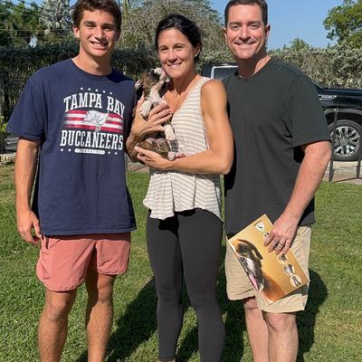 A family happily posing outdoors with their small dog on a sunny day.