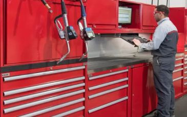 A technician uses a tablet near a large red tool cabinet in a workshop.