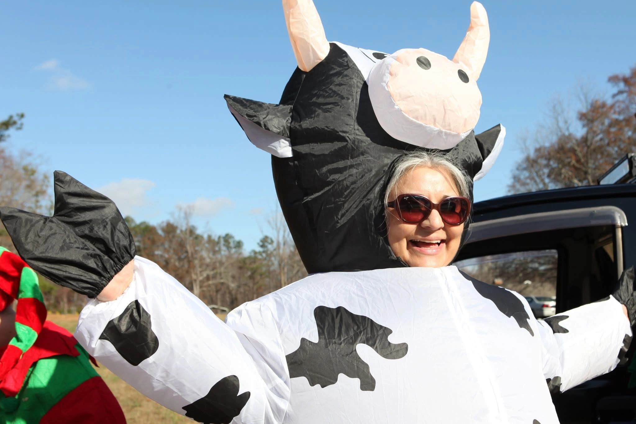 Person in inflatable cow costume smiling outdoors.