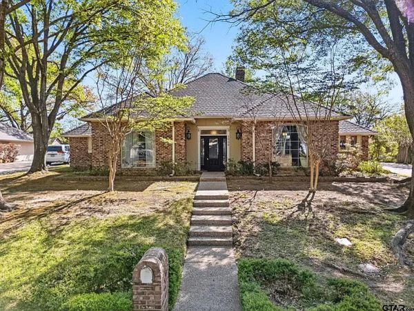 Front view of a brick house with trees and a pathway.