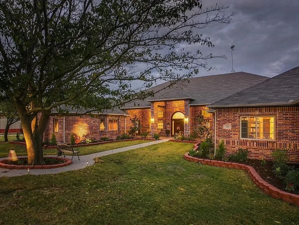 Cozy brick house illuminated at dusk with a landscaped garden and tree.
