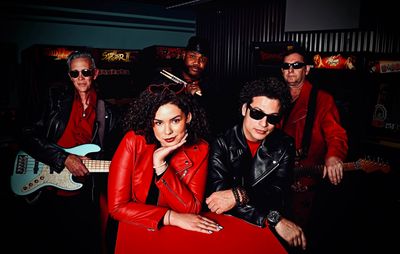 A stylish band of five posing with instruments, wearing black and red leather jackets.