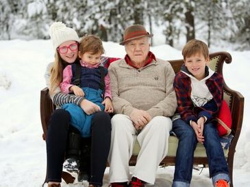 Elderly grandfather surrounded by his grandchildren on a couch in the snow.