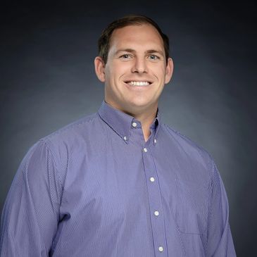 Mark Martindale PA in a blue shirt with a a grey background. 