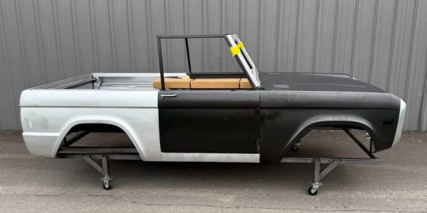 Unfinished car body on wheels beside a gray wall.
