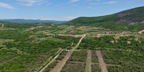 Aerial view of green hills and dirt roads with sparse vegetation under a blue sky.