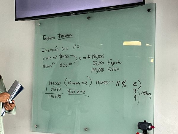 Calculations for land investment with price, area, and payment details on a glass board.
