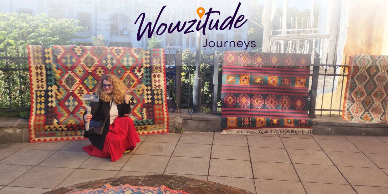 A woman poses with colorful carpets outdoors under Wowzitude Journeys logo.