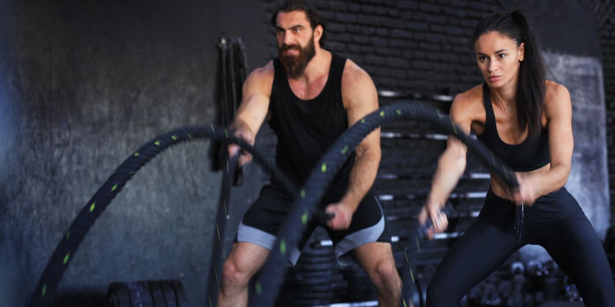 A man and woman intensely working out with battle ropes in a gym.