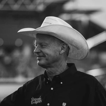 Man wearing a cowboy hat and black shirt smiling outdoors.
