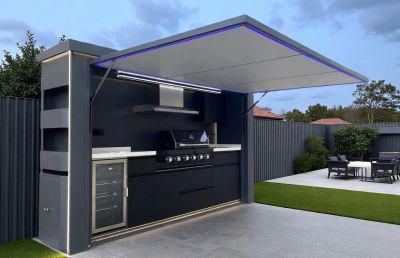 Modern outdoor kitchen with a grill and refrigerator under a retractable canopy.