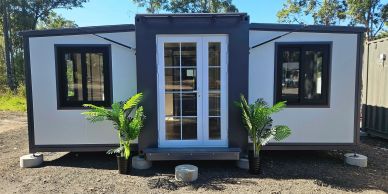 Modern tiny house with white walls and black trim, flanked by two potted plants.