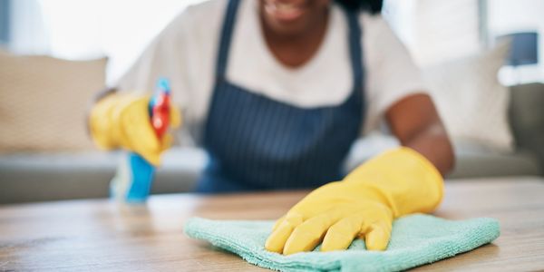 A woman wearing gloves cleaning a countertop, wearing a white t-shirt and blue apron.