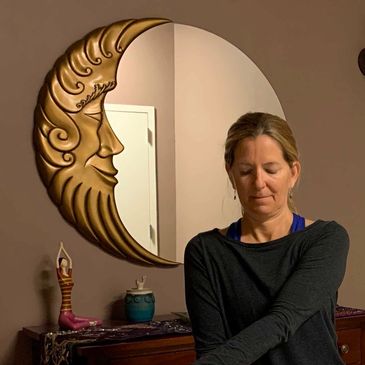 Woman meditating near decorative moon mirror and figurine.