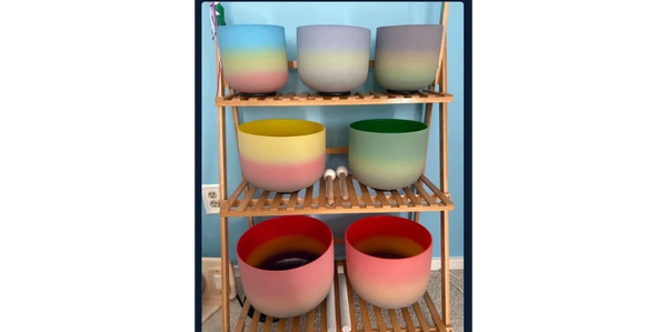Colorful gradient singing bowls on a wooden rack against a blue wall.