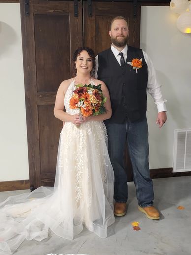 Bride and groom posing indoors in wedding attire with autumn-themed bouquet and boutonniere.