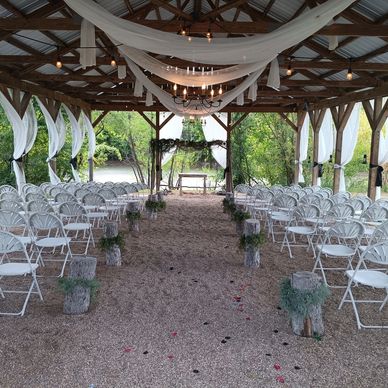 Rustic outdoor wedding setup with white chairs and draped fabric.