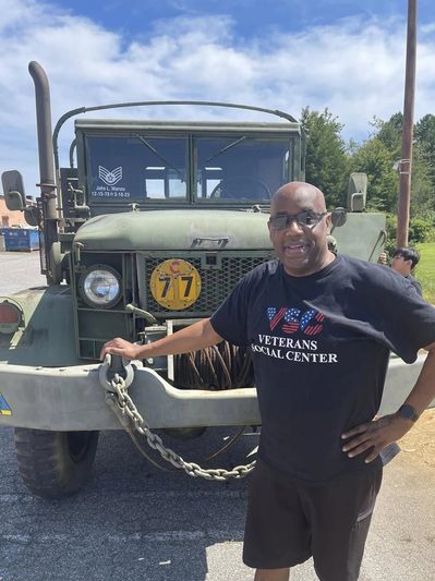 Man posing with a vintage military truck outdoors on a sunny day.