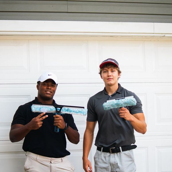 Two men holding window cleaning tools in front of a garage door.