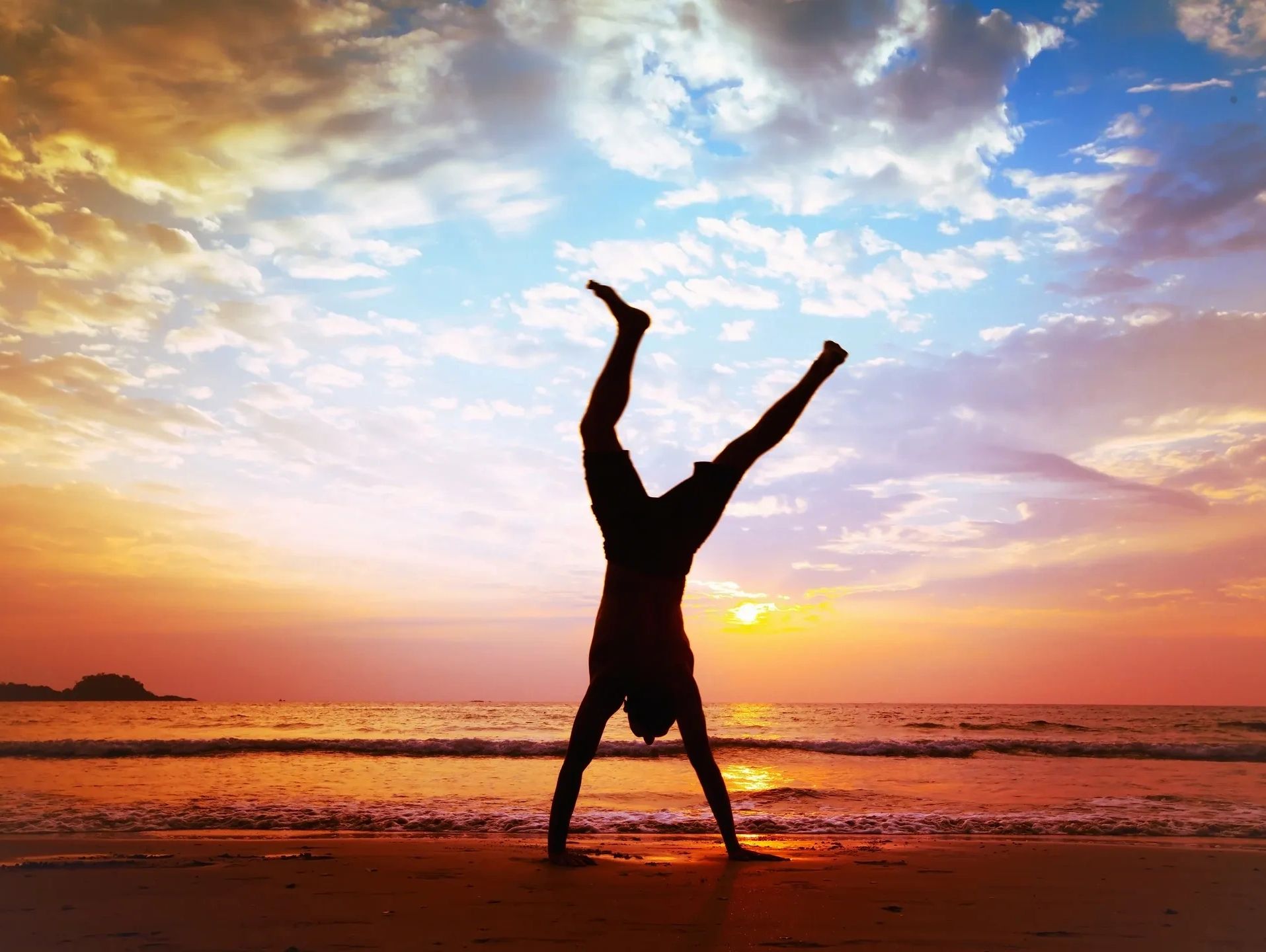Image of a man on the beach doing a handstand with a sunset in the background