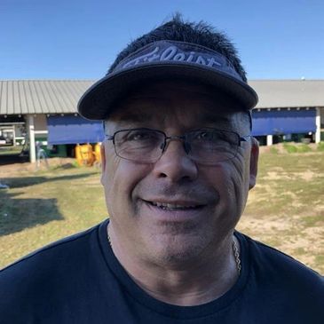 Smiling man wearing glasses and a visor outdoors on a sunny day.