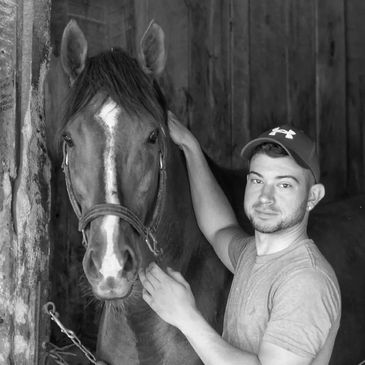 A man in a cap gently pets a horse in a stable.