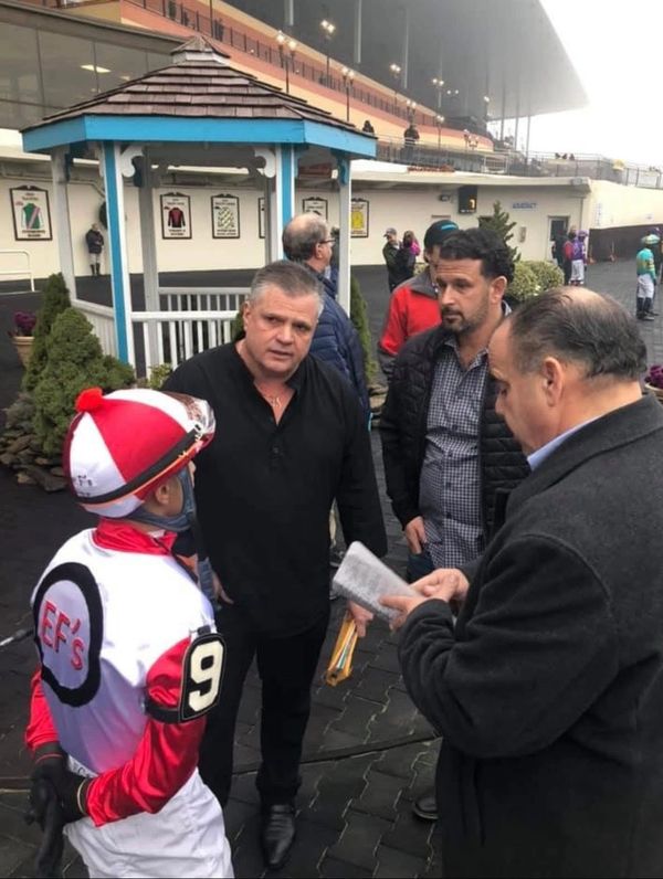 A jockey in racing gear talks with three men at a racetrack.