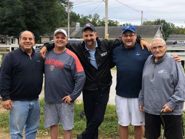 Group of five men posing outdoors, smiling and relaxed.