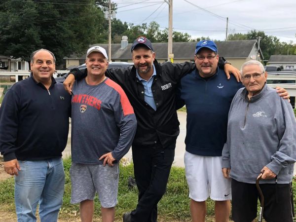 Group of five men posing outdoors, smiling and relaxed.
