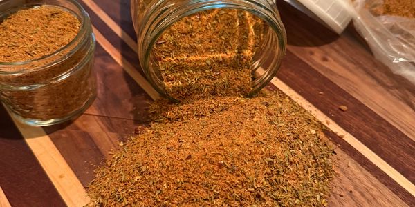 Spilled seasoning from a glass jar on a wooden cutting board.