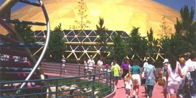Visitors walk near a large yellow geodesic dome at a park or exhibition.