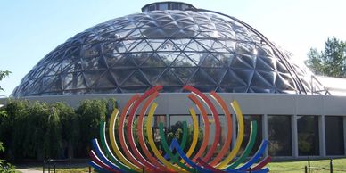 A large geodesic dome with a colorful sculpture in front.
