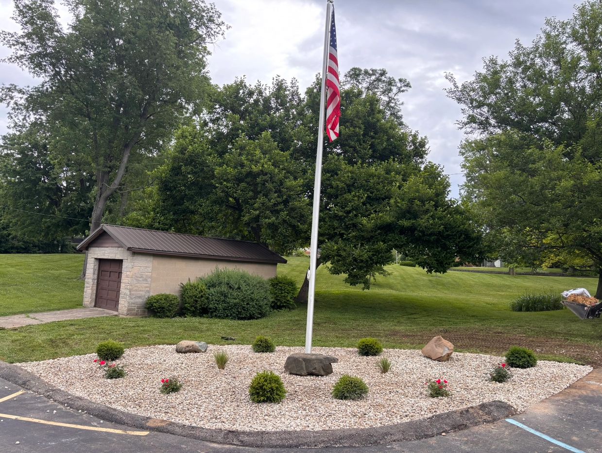 American flag on a pole surrounded by a garden with bushes and rocks.